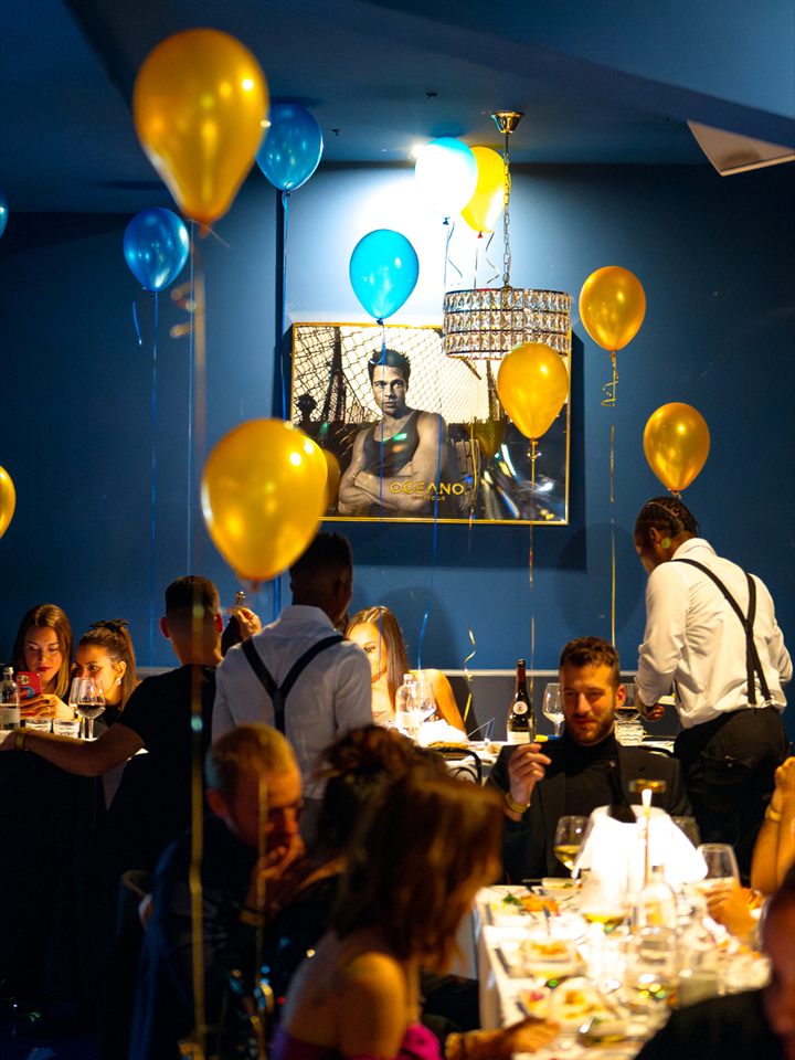 La sala allestita con palloncini oro e blu e i camerieri che servono ai tavoli